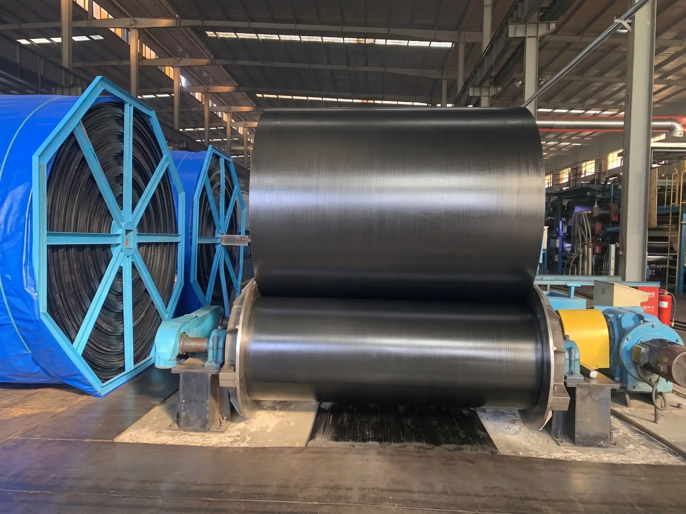 Industrial rubber conveyor belt being processed on calendering machine with large rollers in manufacturing factory